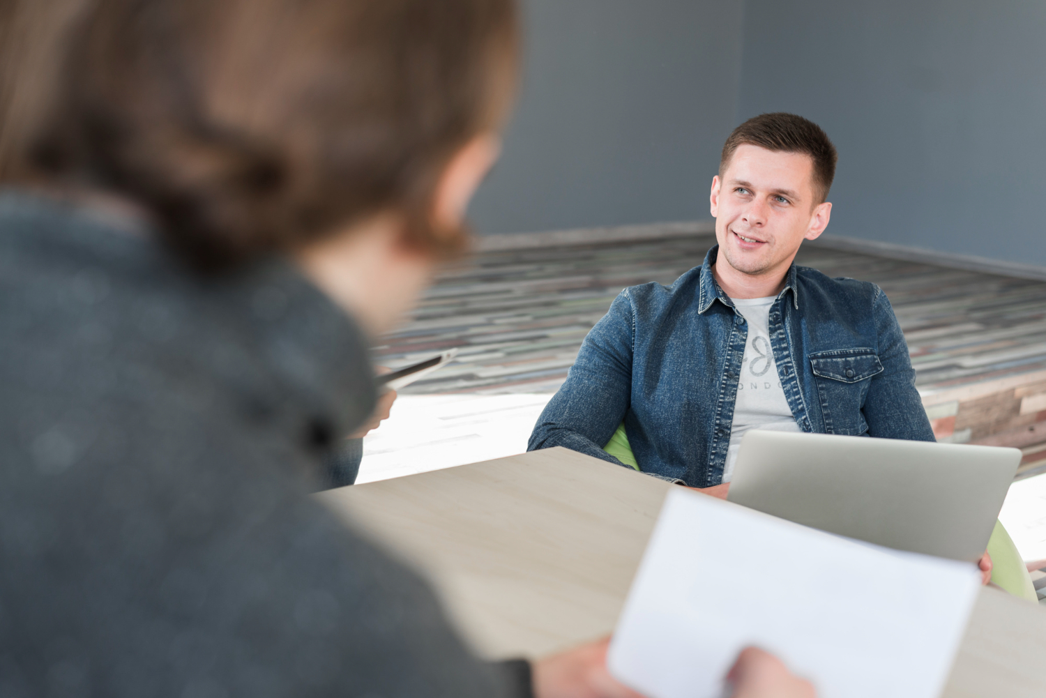 A side-profile view of two men sitting together and talking in a casual office setting.